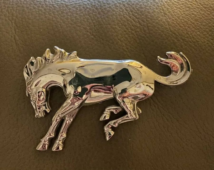 Chrome Ford Bronco bucking-horse emblem resting on brown leather, a mark of the Buck Buck Bronco tradition